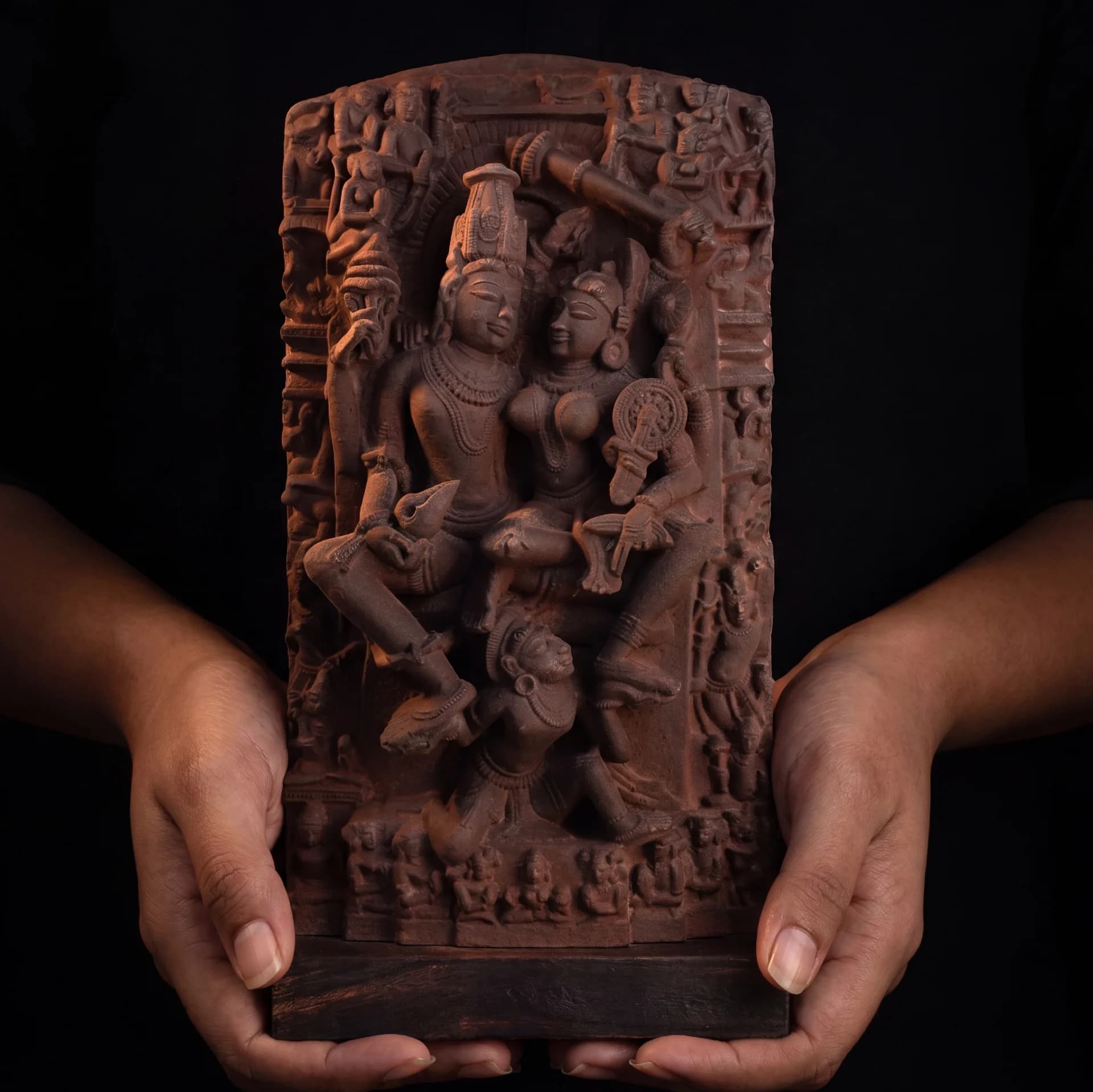 A pair of hands holding a detailed Lakshmi Narayan Sculpture, a hand-finished stone-style replica featuring intricate 12th-century relief carvings.