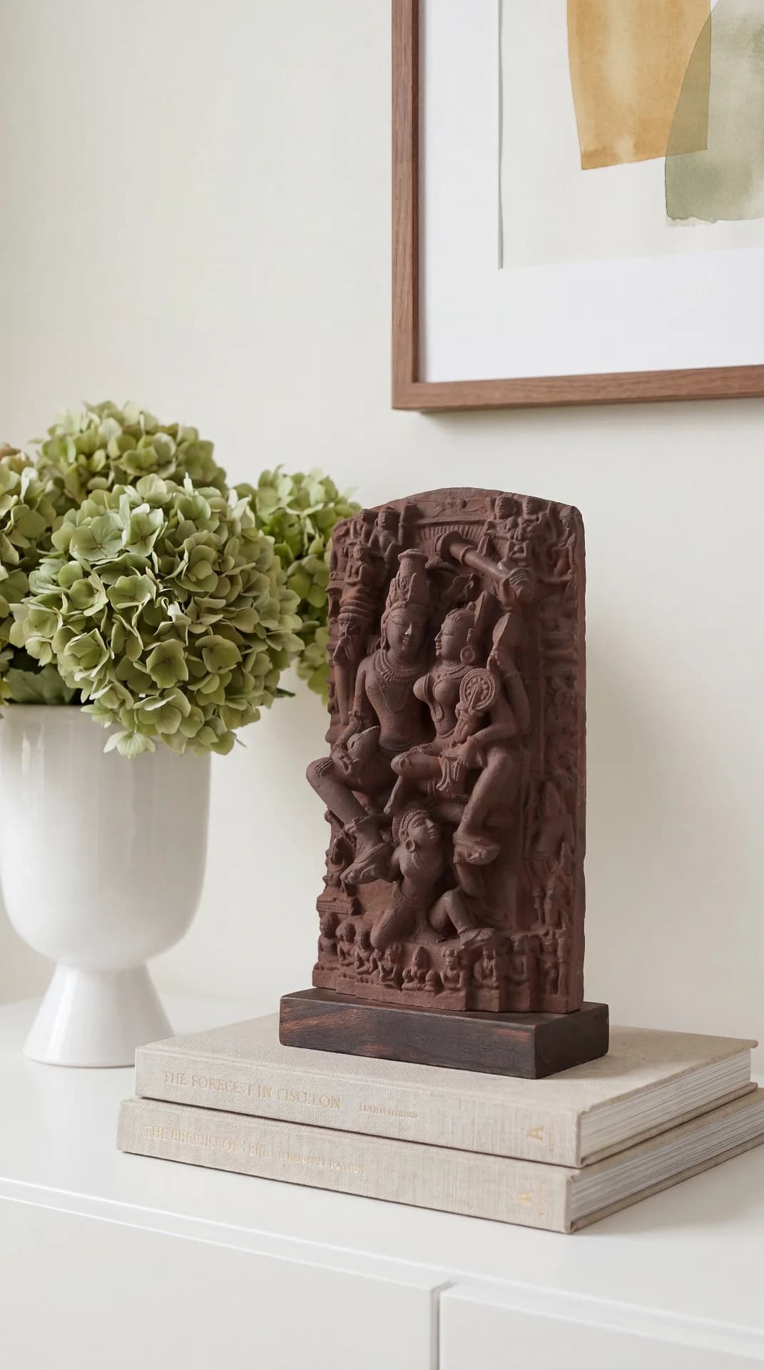 The Lakshmi Narayan Sculpture 9 Inch sits on stacked books, showcasing its intricate hand-finished terracotta-style relief detail in a home setting.