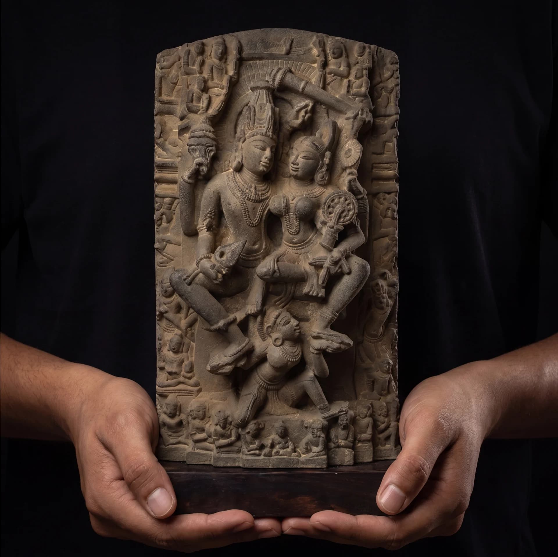 A pair of hands holds a detailed Lakshmi Narayan Sculpture, a stone-finish replica featuring intricate 12th-century style carvings.