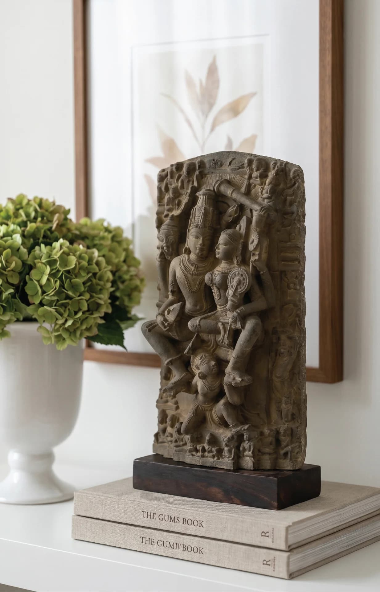 A hand-finished stone Lakshmi Narayan Sculpture displayed on stacked books, showcasing intricate 12th-century style relief carvings.