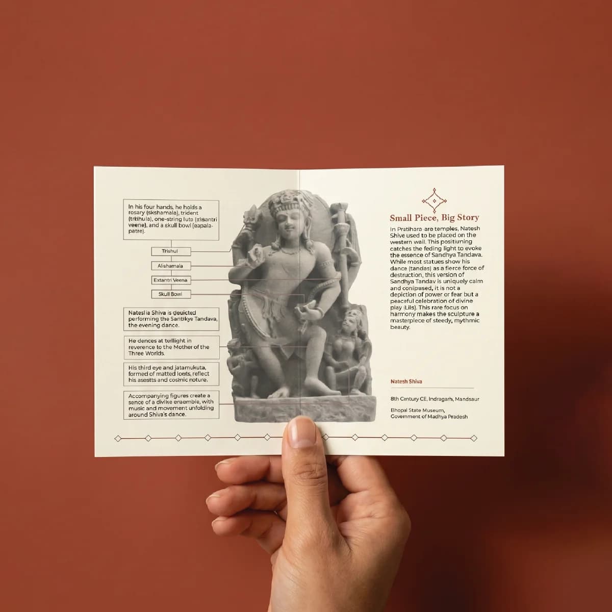 A hand holds an informational brochure about the Natesh Shiva Sculpture, featuring detailed annotations of this stone composite replica.