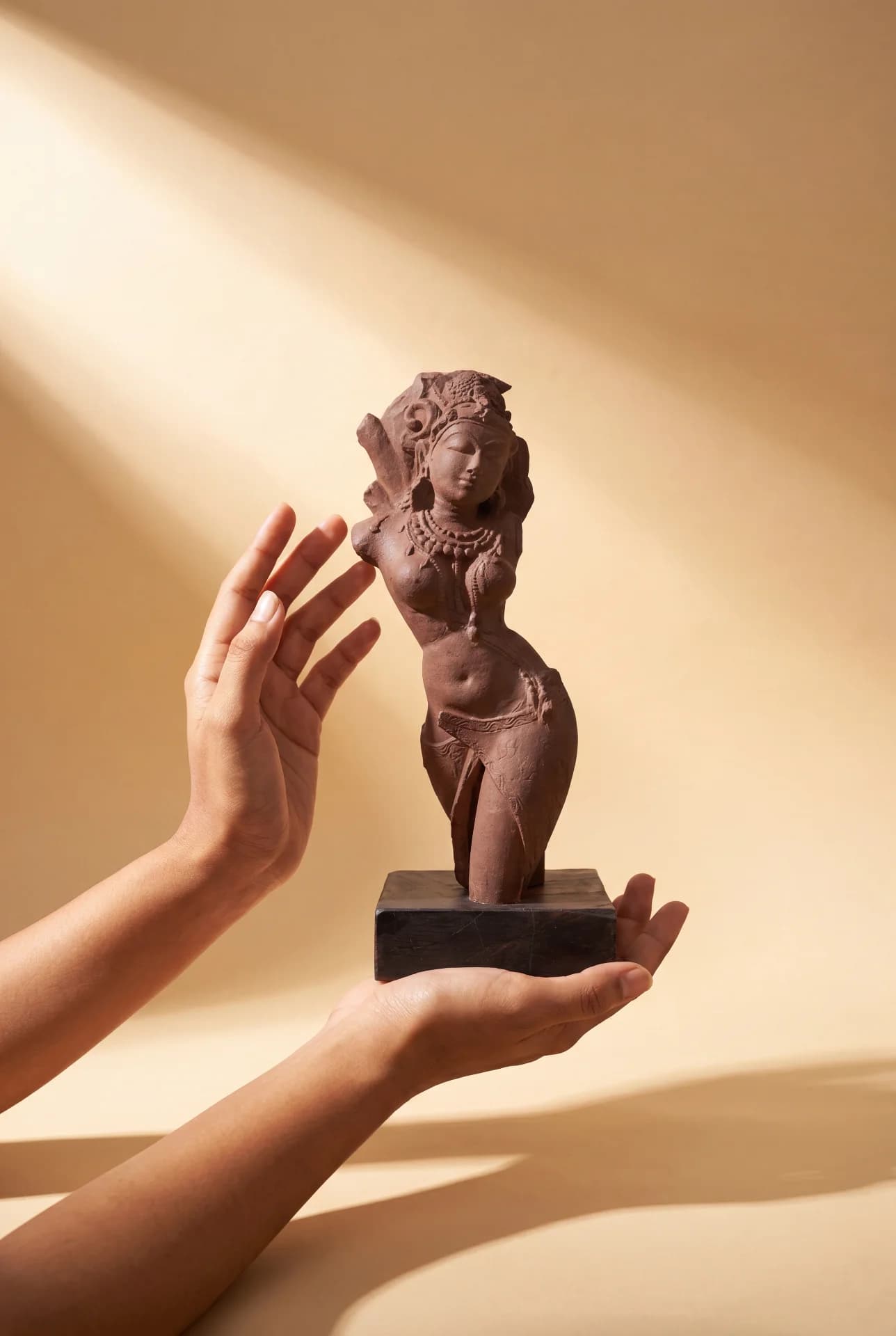 A pair of hands gently cradles the Salabhanjika Sculpture, a stone composite replica featuring intricate carvings on a wooden base.