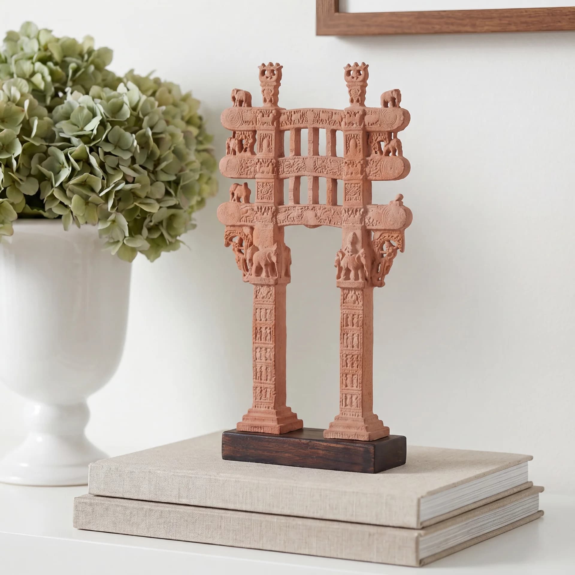 A Sanchi Torana Gateway Miniature made of stone composite, standing on a wooden base atop stacked books.