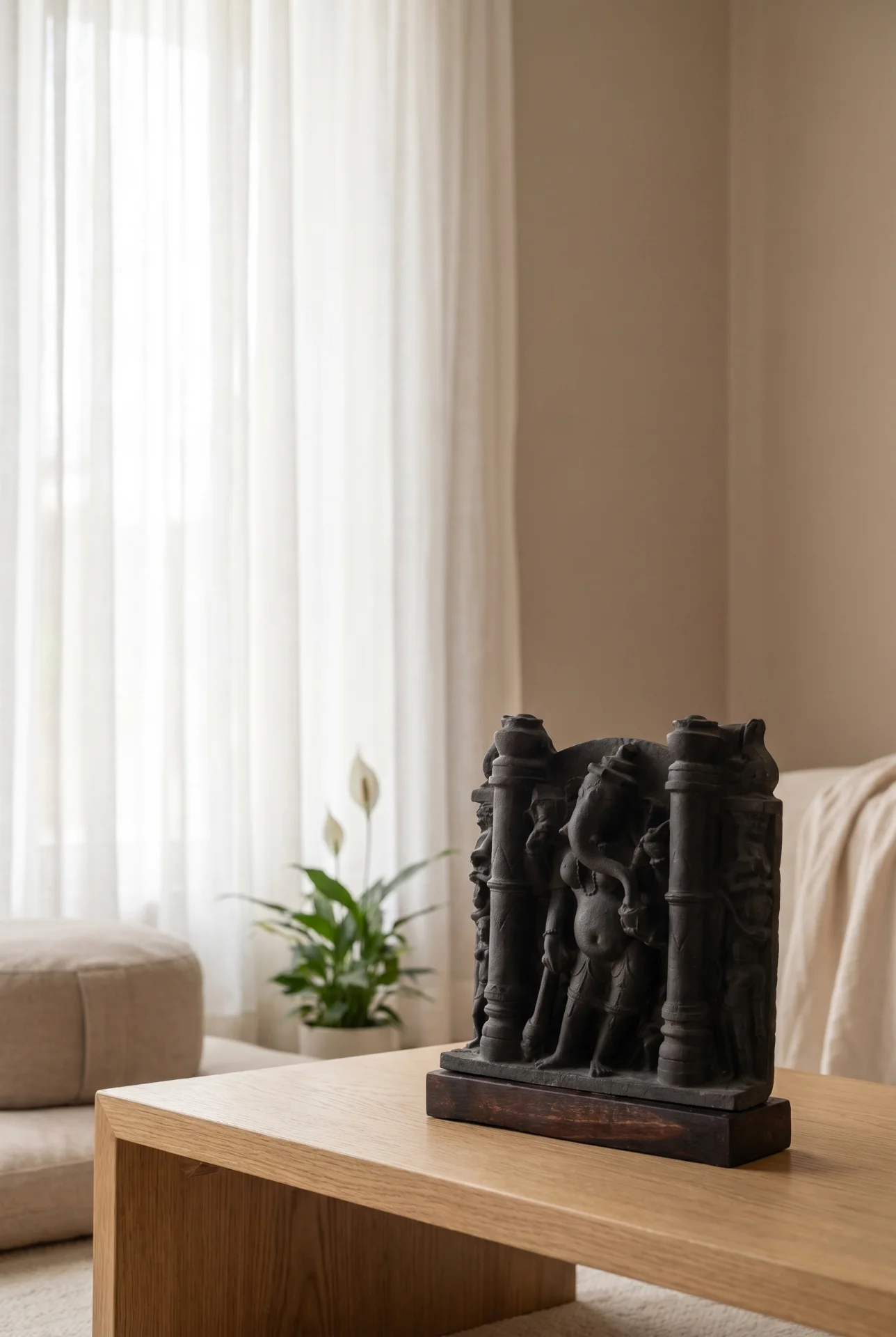 A dark stone Vinayaki Sculpture replica displayed on a wooden table in a bright, minimalist living room setting.
